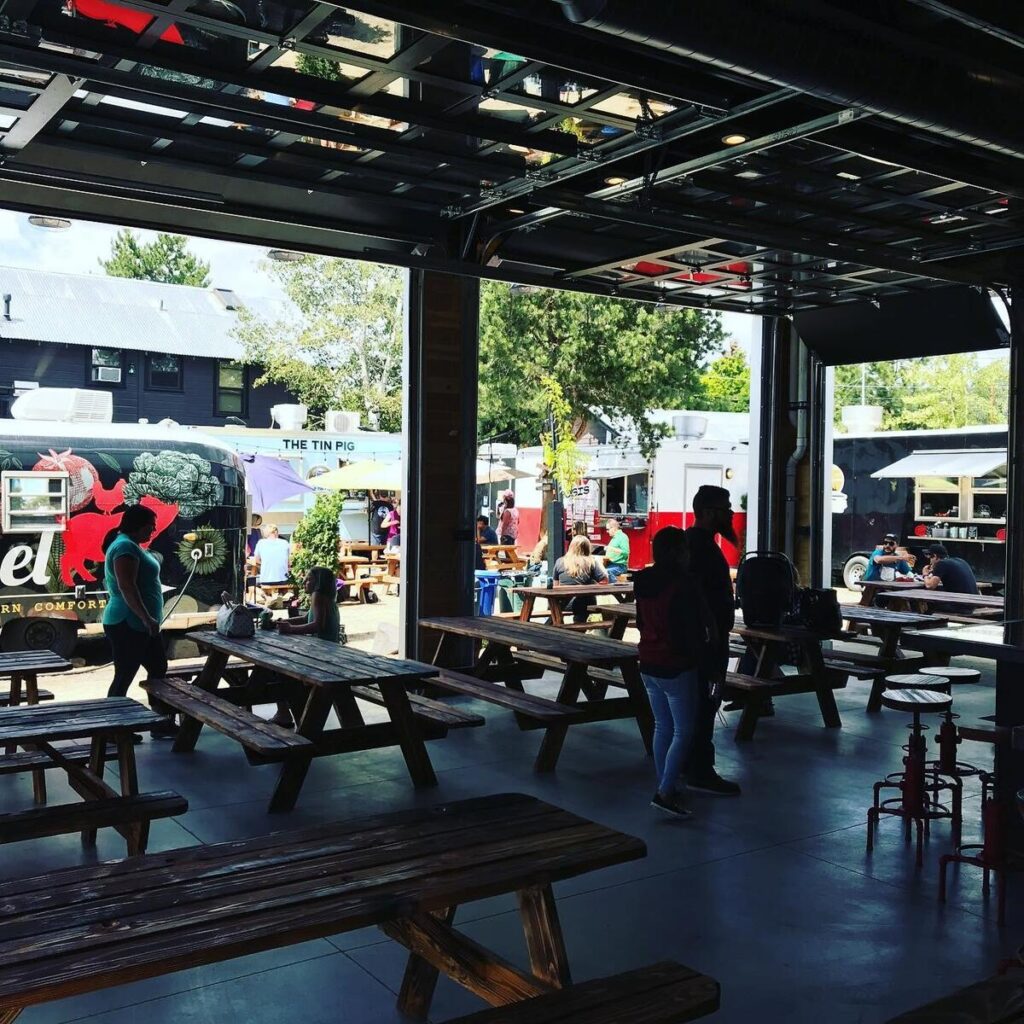Picnic tables and food carts at a Bend food cart lot, seen from the covered seating pavilion