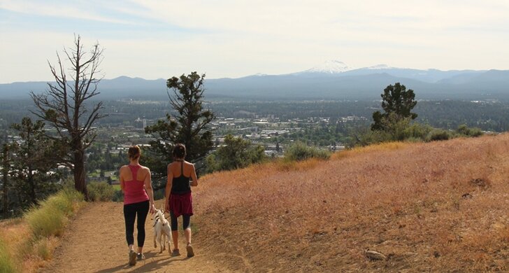 Hikers and a dog on the Pilot Butte trail with Bend and Mt. Bachelor below